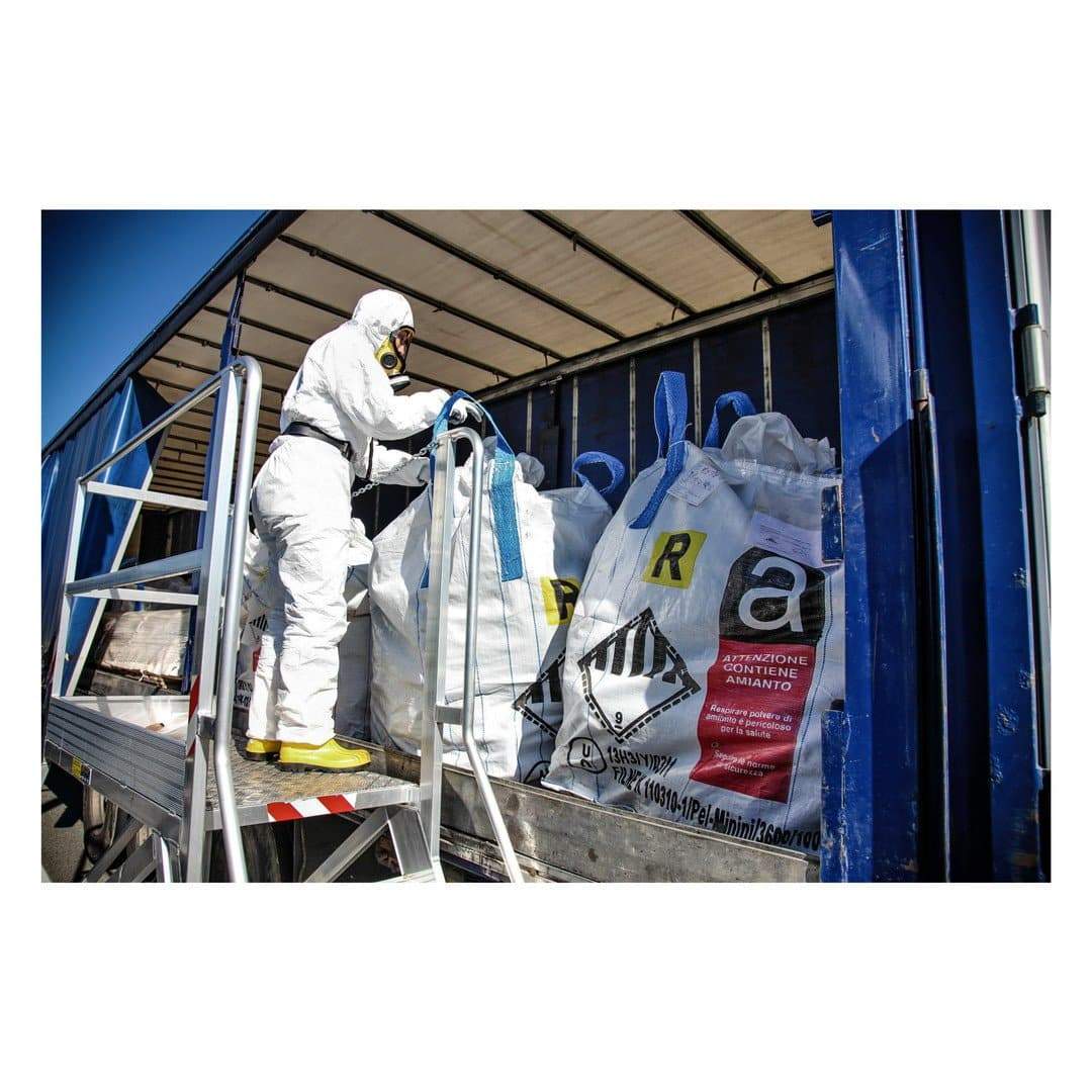 Worker in protective suit loading asbestos waste bags.