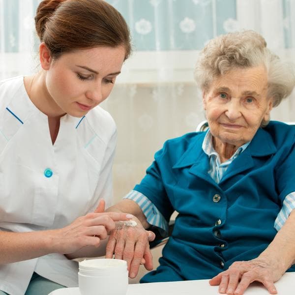 Perineal skincare for elderly woman, nurse applying cream.